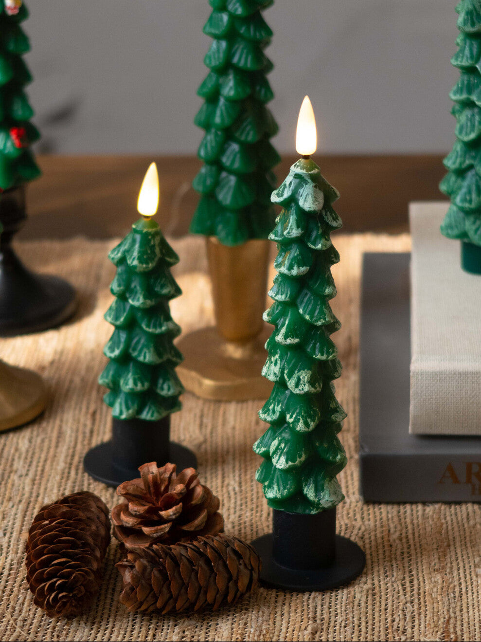 Decorative candles shaped like Christmas trees on a textured surface with pine cones.