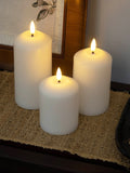 Three white candles with flame on a textured surface, possibly a table or mat.