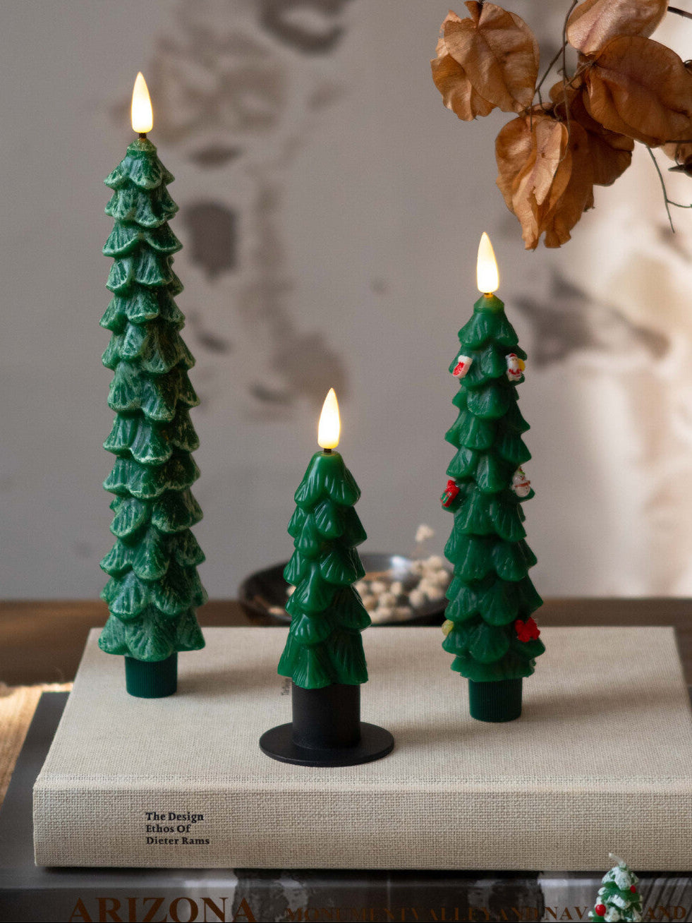 Three green Christmas tree-shaped candles on a book with a blurred background