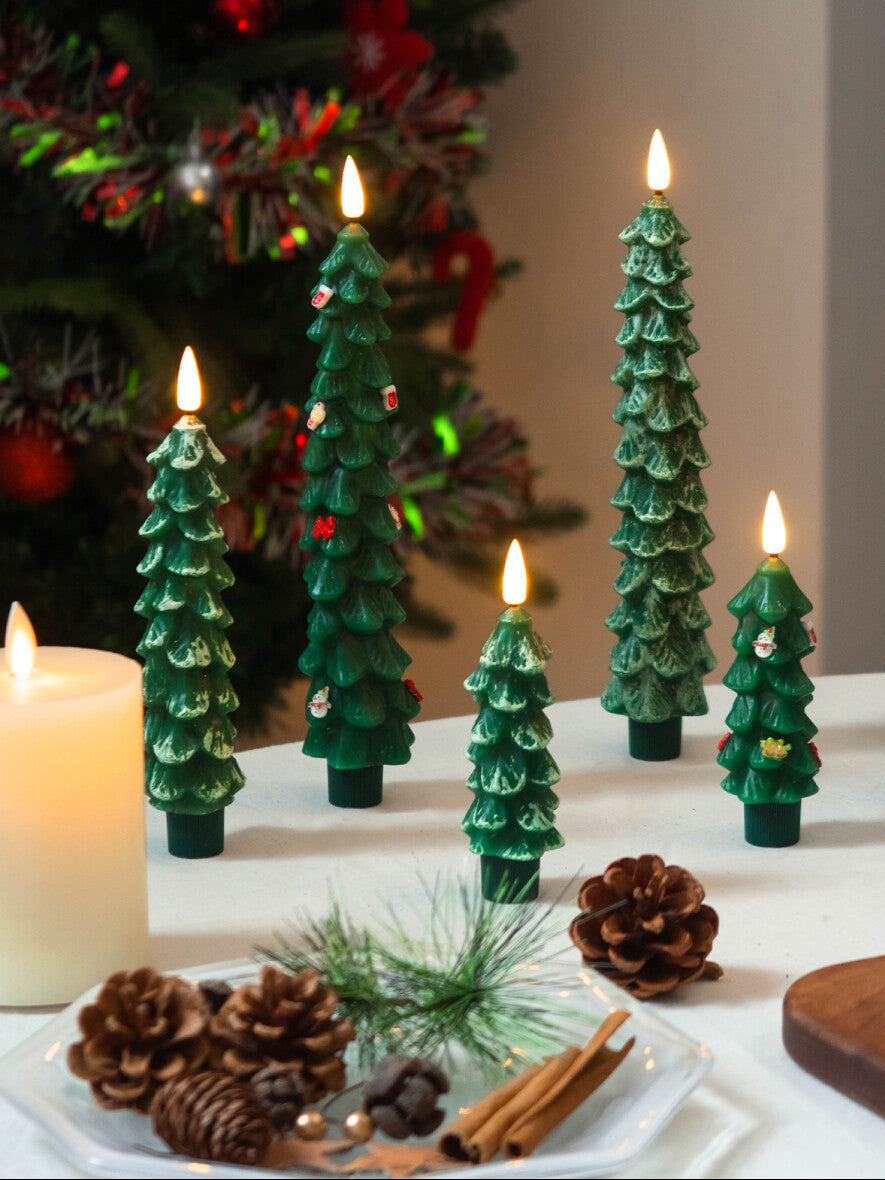 Decorative Christmas tree-shaped candles on a table with a Christmas tree in the background.