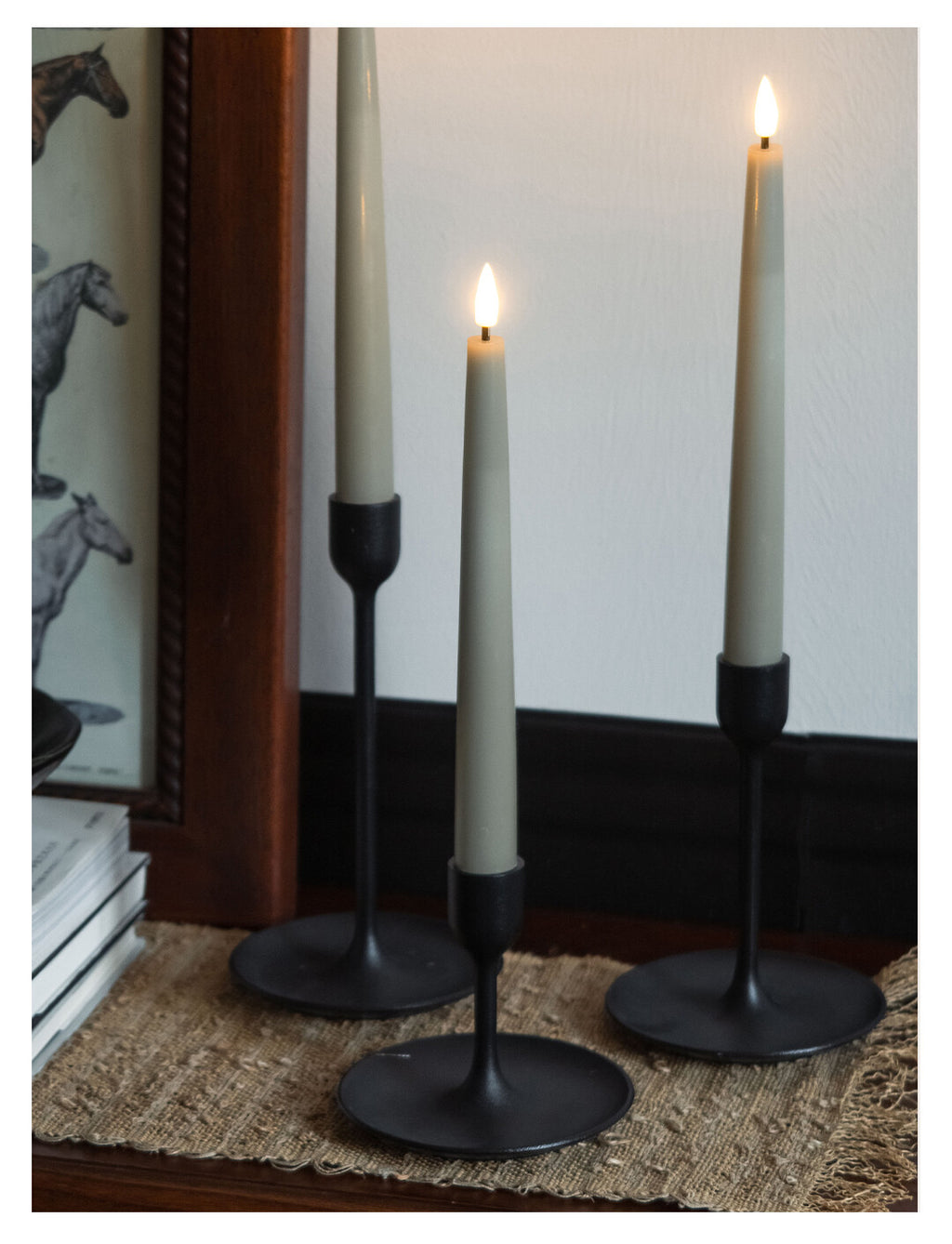 Three black candle holders with lit candles on a textured surface.