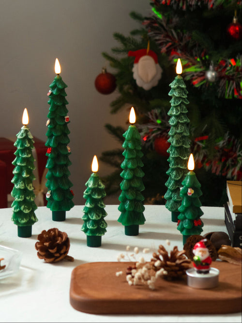 Decorative candles shaped like Christmas trees on a table with a Christmas tree in the background.