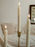 Three lit candles in front of a white sofa with a decorative frame on the wall.