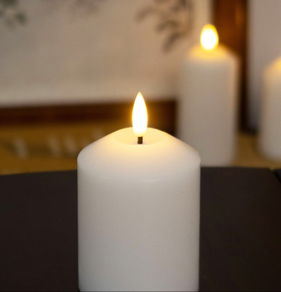 White candle with a lit flame on a dark surface, with blurred candles in the background.