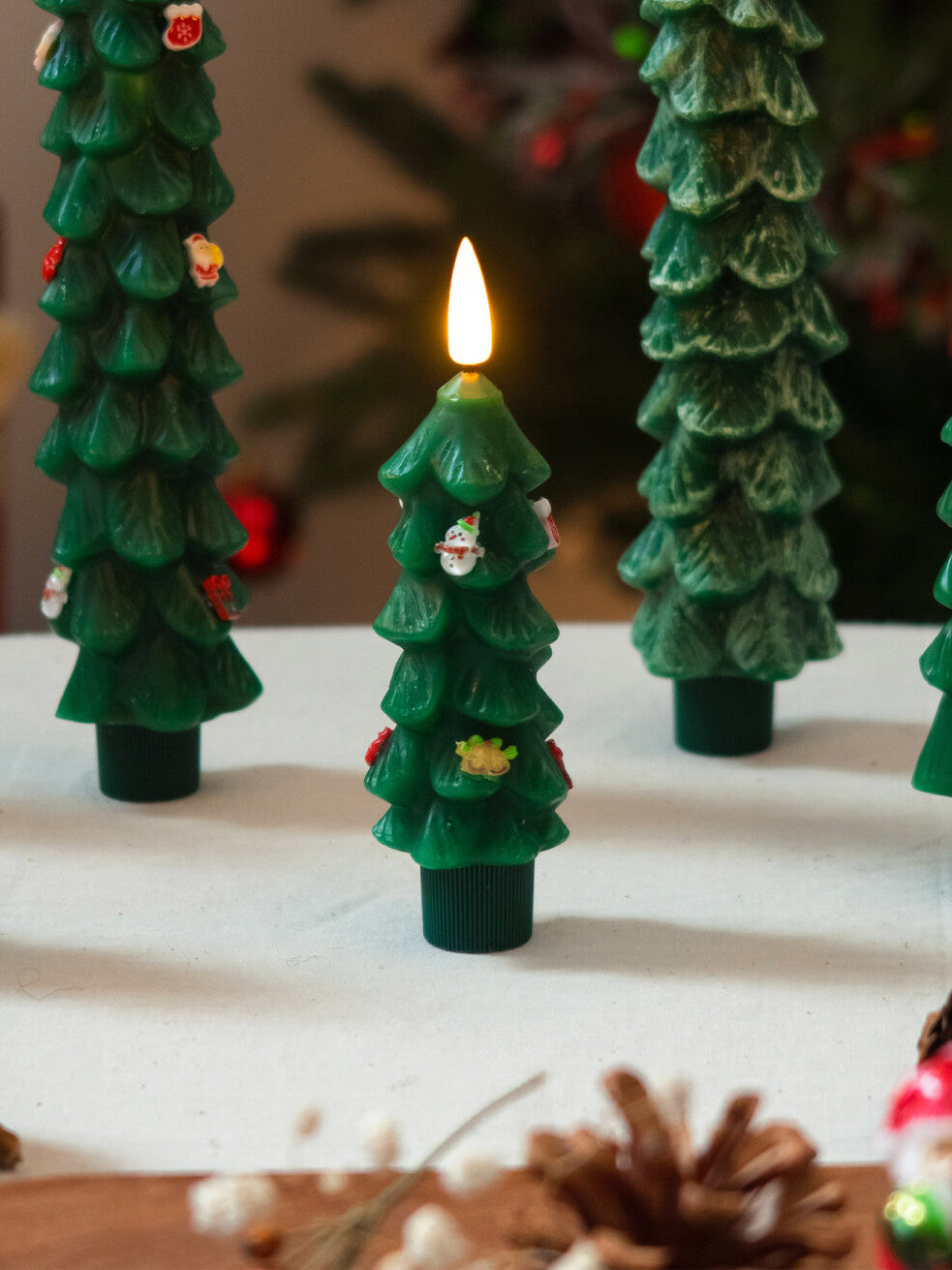 Decorative Christmas tree candles with a lit candle in the center on a white surface.