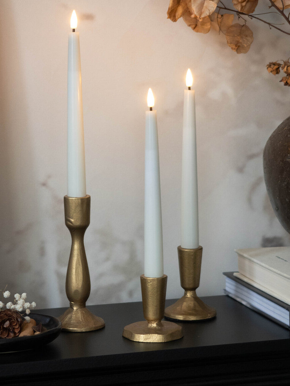 Three white candles in gold candle holders on a dark surface with a blurred background