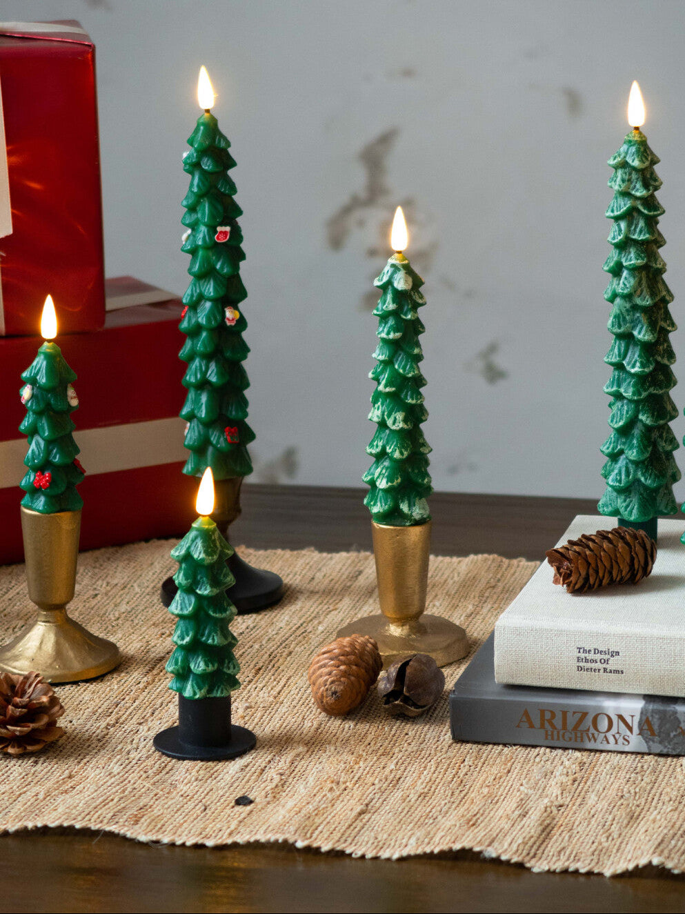 Decorative Christmas tree candles on a table with books and pinecones.