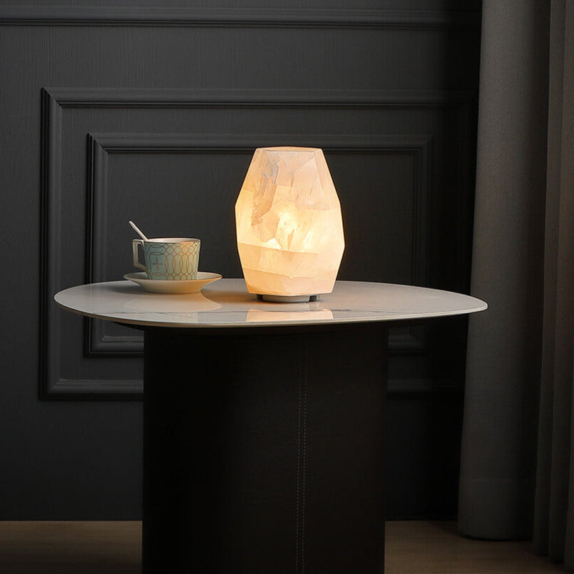 Small round table with a lamp and cup against a dark paneled wall.