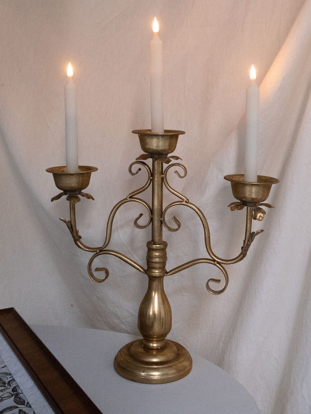 Gold candelabra with three lit candles against a white curtain background