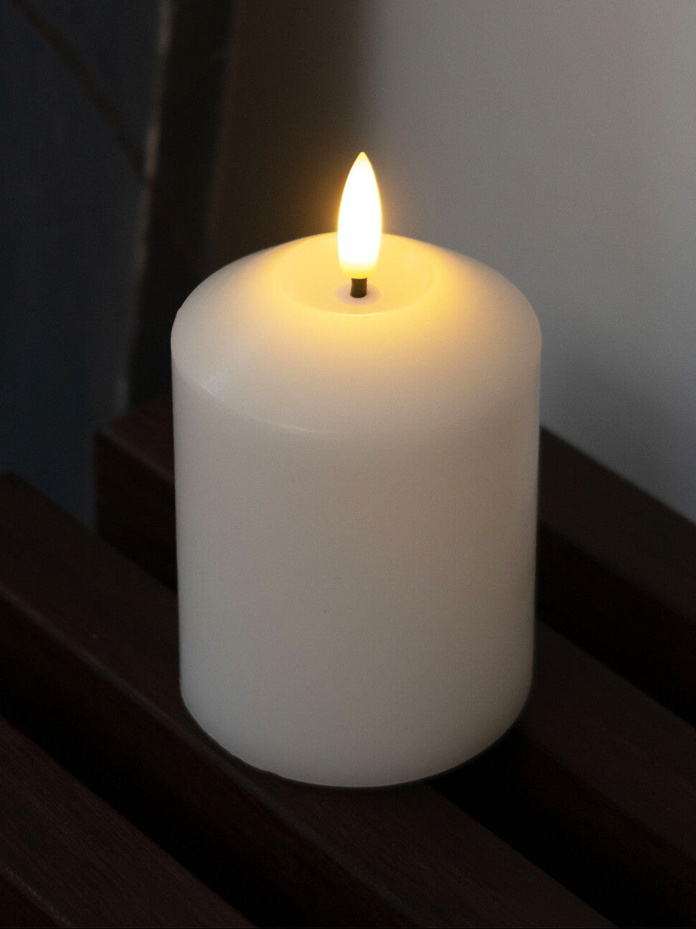 White candle with a small flame on a dark surface