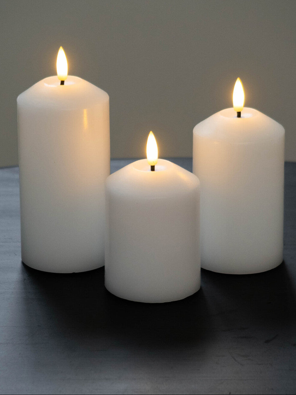 Three white candles with flames on a dark surface and gray background