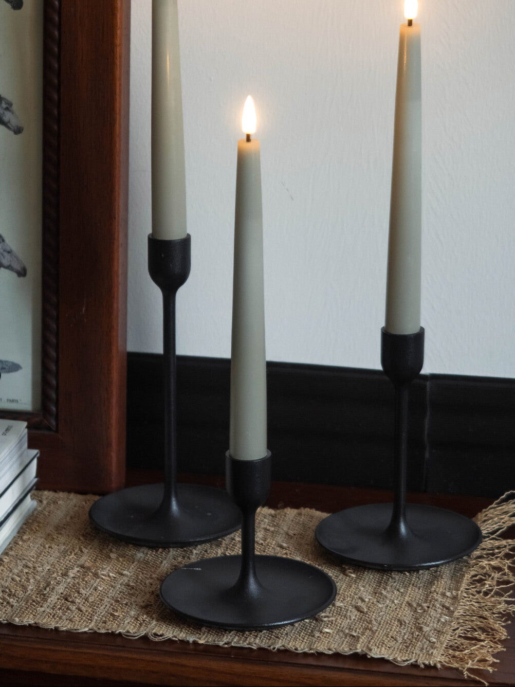 Three black candle holders with lit candles on a textured surface.