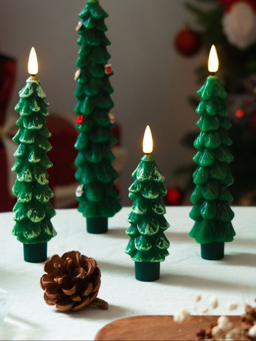 Set of green Christmas tree-shaped candles with lit flames on a white surface.