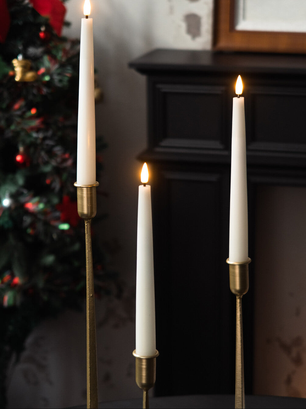 Three lit candles in brass candlesticks with a festive background